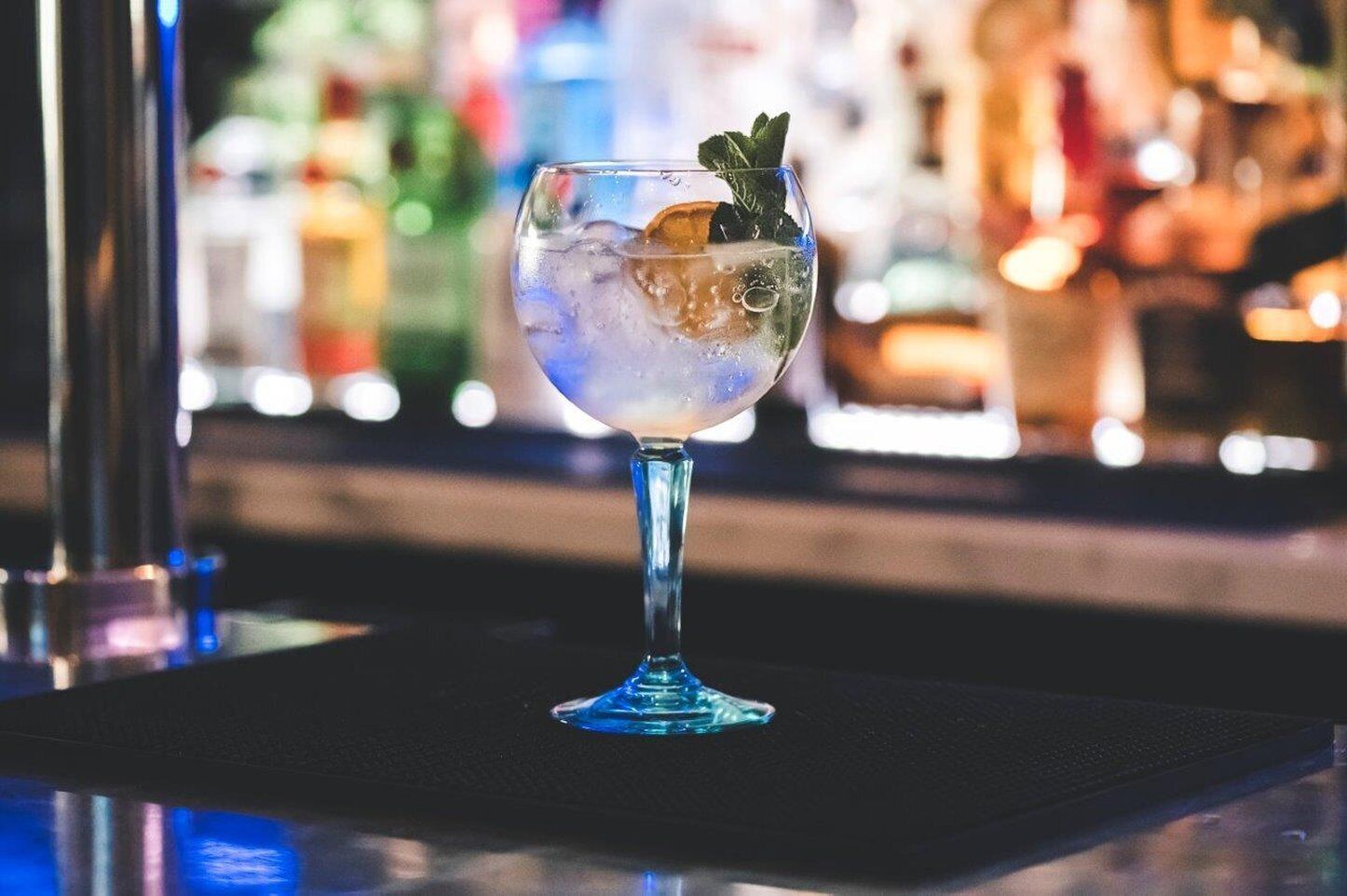 Um copo de cocktail com gelo e folhas de hortelã sobre um balcão de bar.