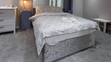 A bedroom with a bed, a bedside table, a lamp, a dresser, and a mirror.