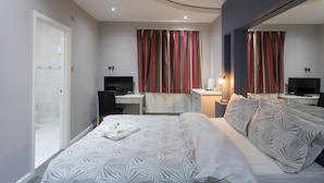 A modern hotel room with a large bed, a desk, a chair, a TV, and a mirror. - High Bank Hotel (Leeds)