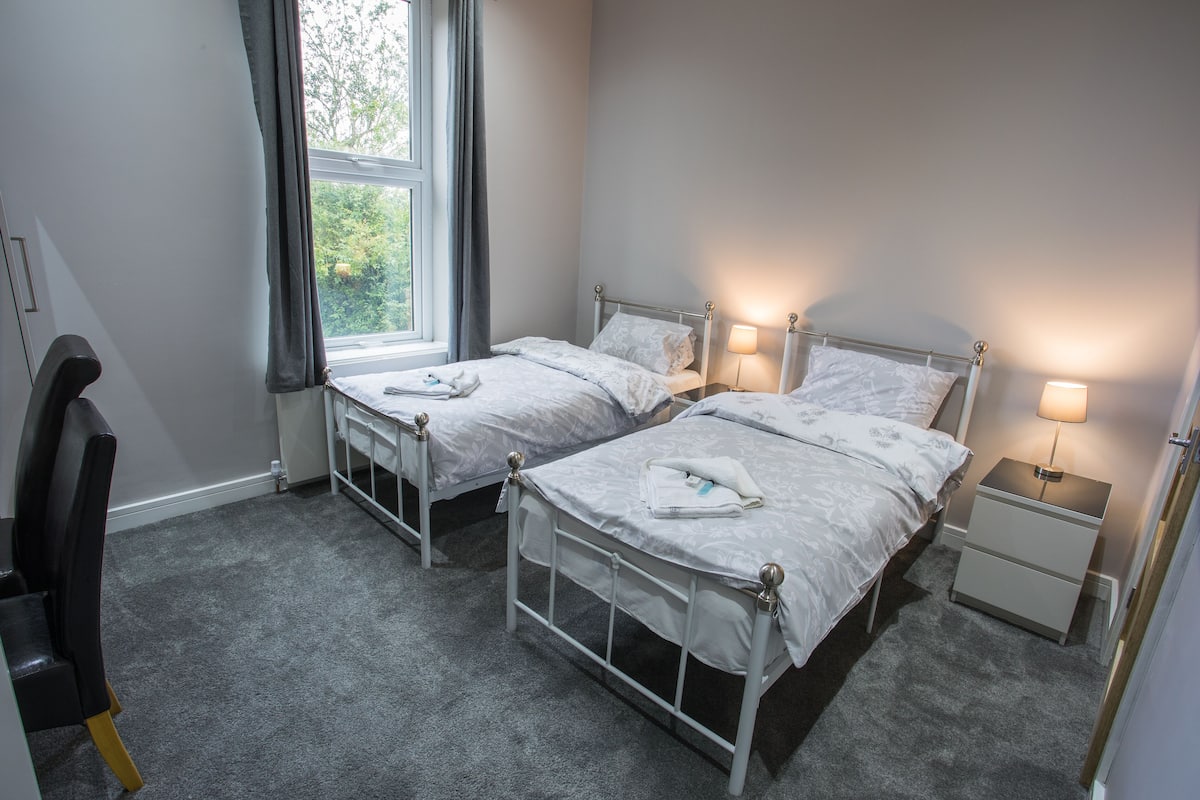 Une chambre double avec deux lits, une table de chevet, une chaise et une fenêtre avec des rideaux.