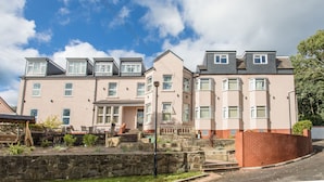 A multi-story residential building with a flat roof, multiple windows, and a stone wall in the foreground. - High Bank Hotel (Leeds)
