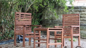 A wooden bench and table set in a garden area with a stone wall and dense foliage in the background. - High Bank Hotel (Leeds)