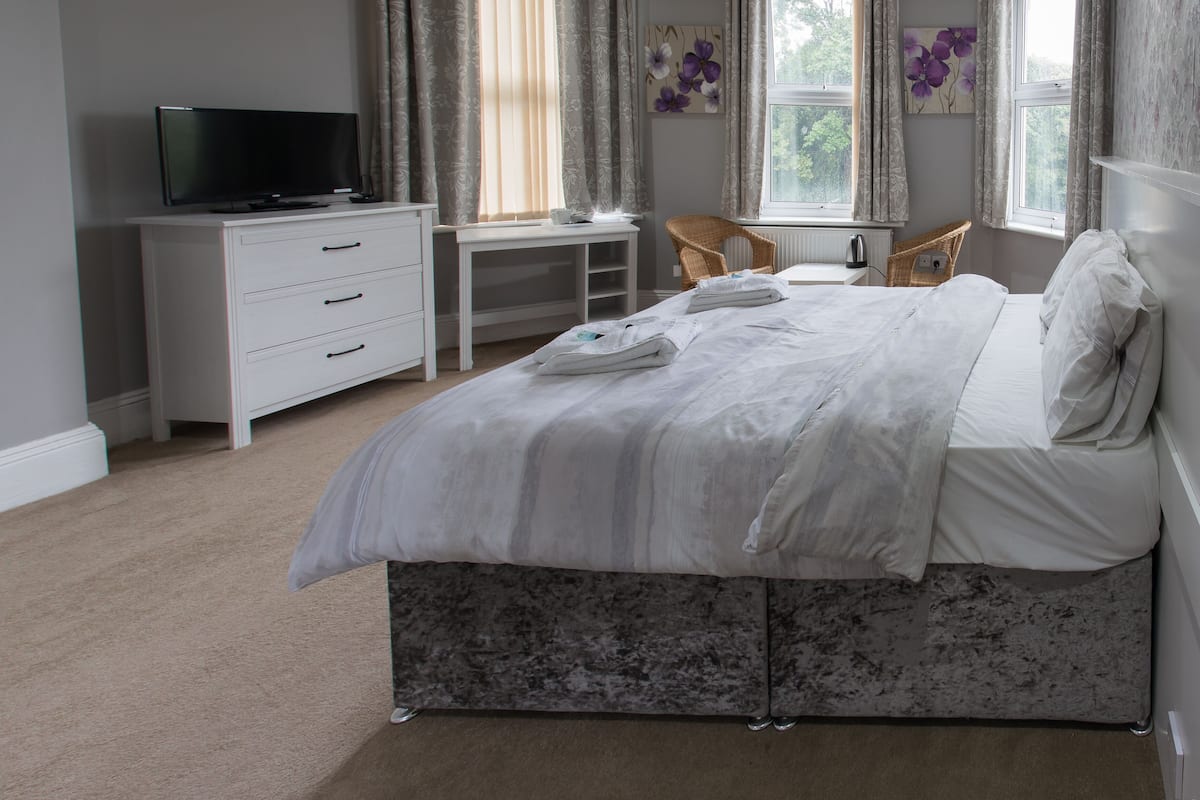 Une chambre à coucher avec un lit, un bureau, une chaise, un téléviseur et une fenêtre avec des rideaux.