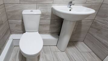 Een badkamer met een toilet en een wastafel, beide wit, tegen een betegelde muur.
