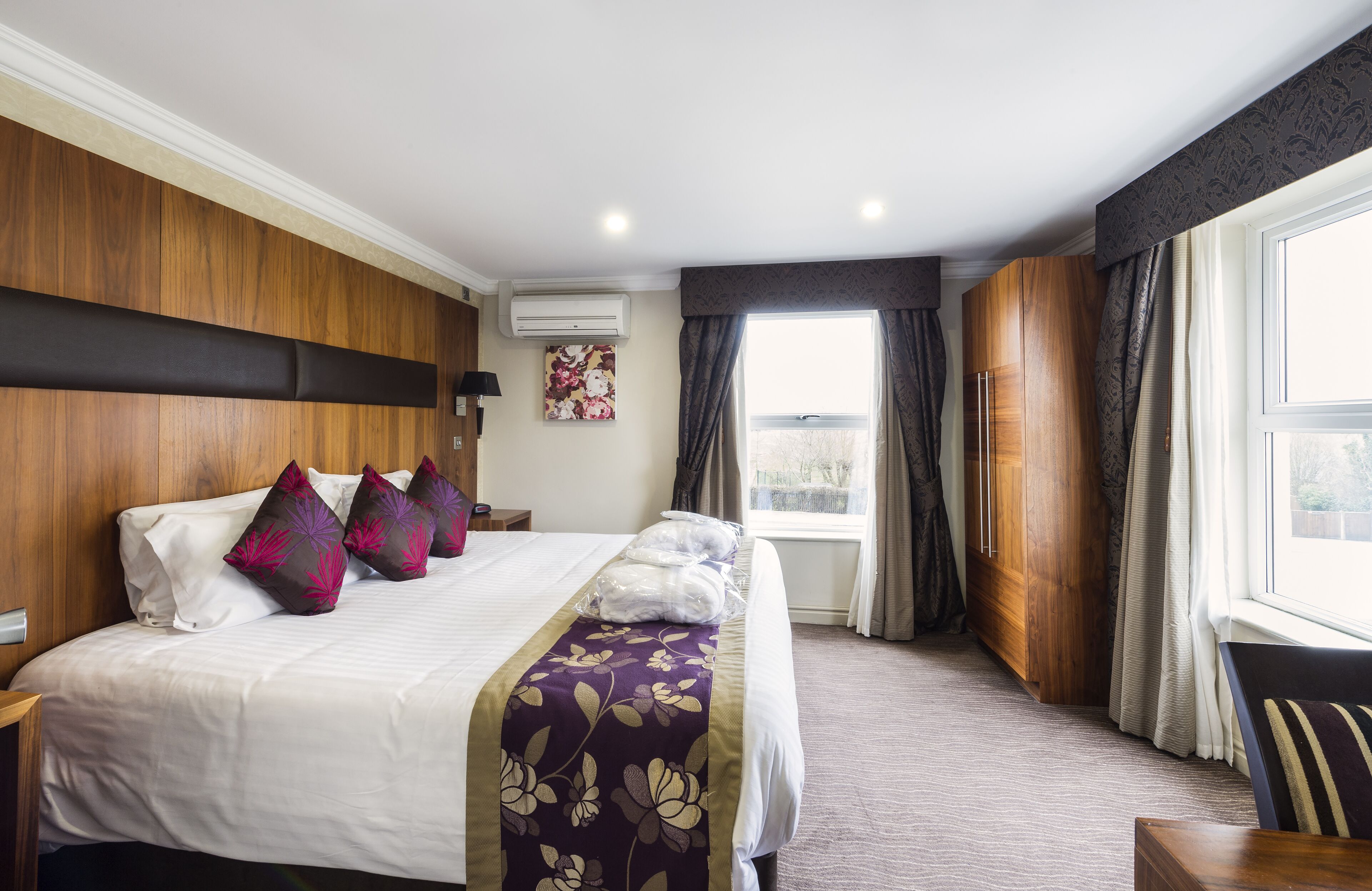 A hotel room with a large bed, wooden headboard, a window with curtains, and a view of the outside.