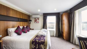 A hotel room with a large bed, wooden headboard, a window with curtains, and a view of the outside.
