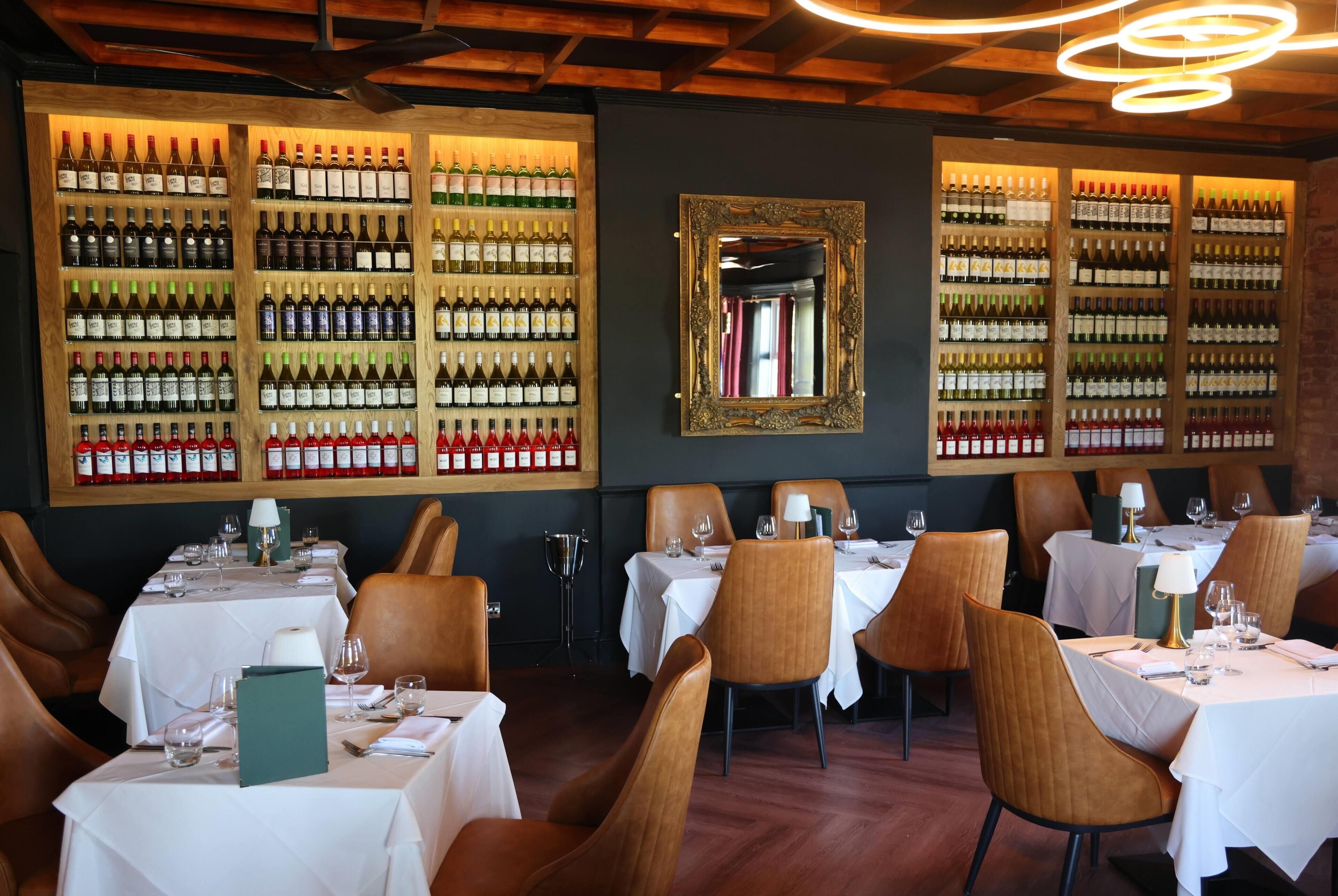 A restaurant interior with multiple tables, chairs, and a wine rack displaying various bottles.