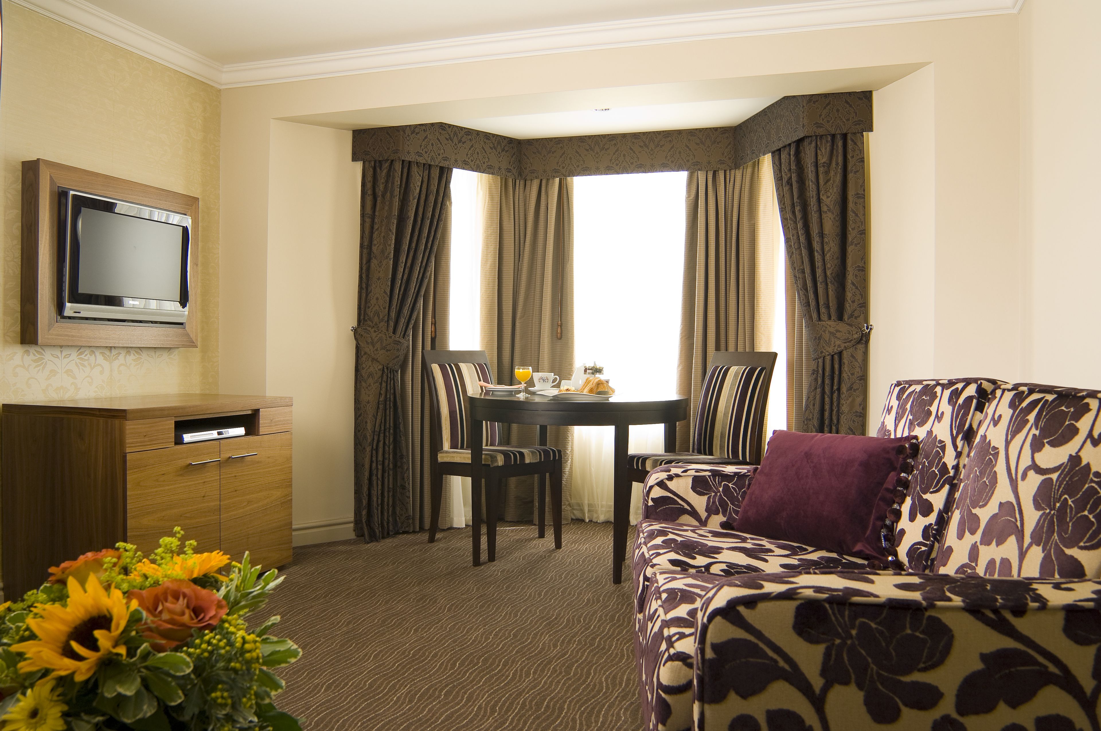 Ein Hotelzimmer mit Essbereich, einer Couch, einem Fernseher und einer Blumenkomposition.