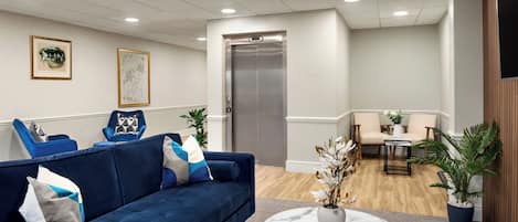 A modern lobby with a blue sofa, a marble coffee table, and a reception desk.