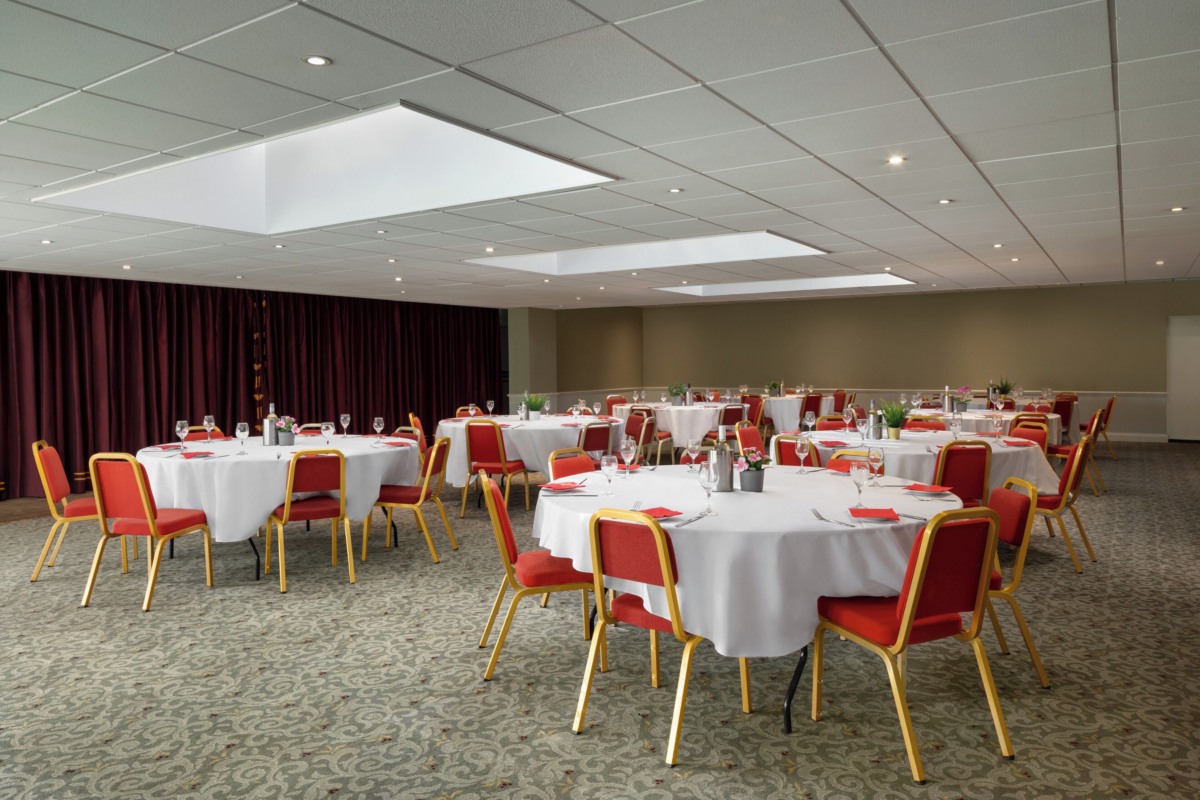 A conference room with multiple round tables, each set with white tablecloths and red chairs.