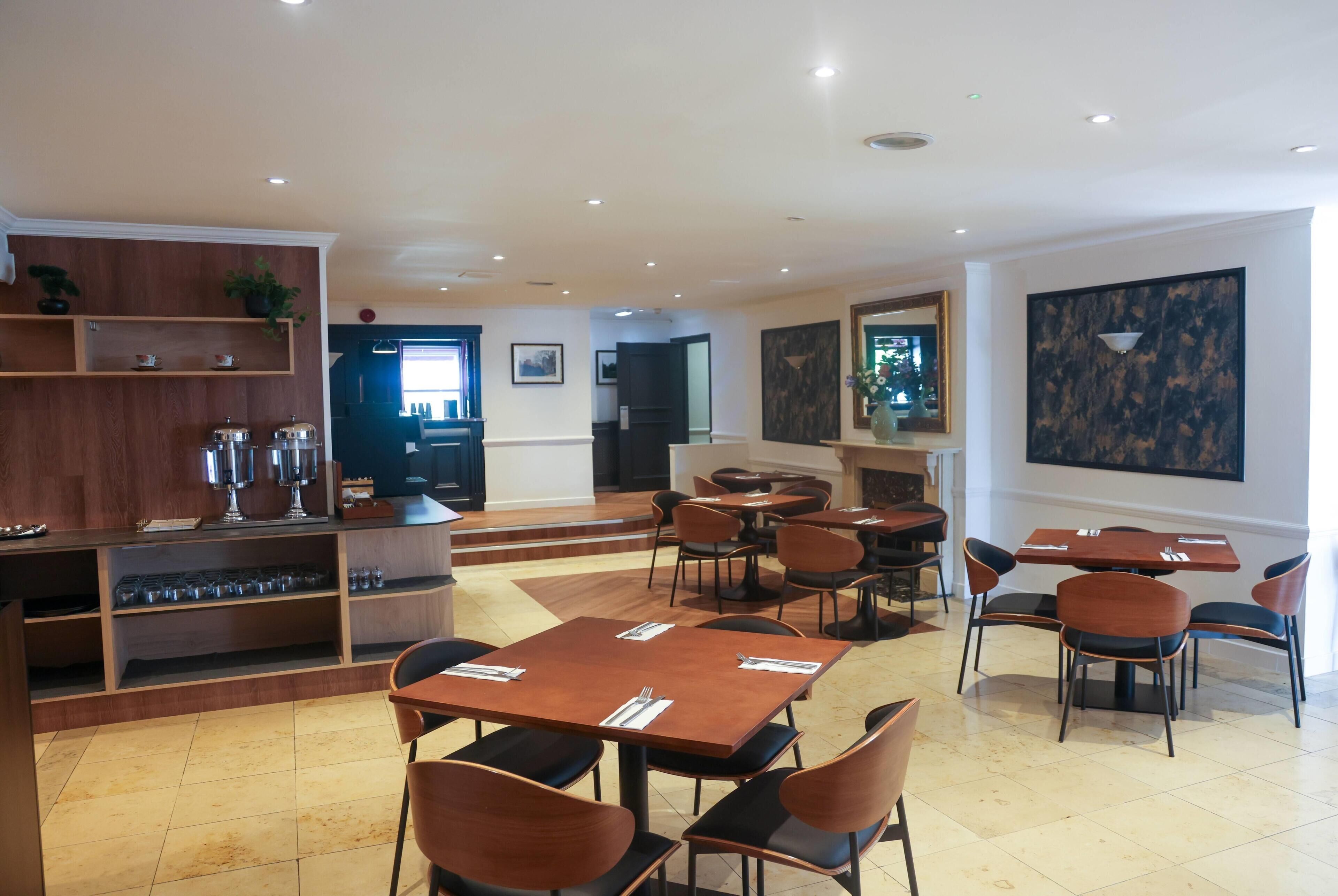 A restaurant with multiple tables and chairs, a bar area with shelves, and a counter with glasses.