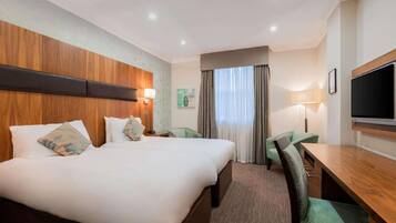 Ein Hotelzimmer mit einem großen Bett, einem Schreibtisch, zwei Stühlen, einem Fernseher und einem Fenster mit Vorhängen.