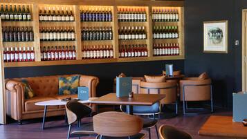 Zona de bar con varias opciones de asiento, incluyendo un sofá y mesas, y una pared llena de botellas de vino.