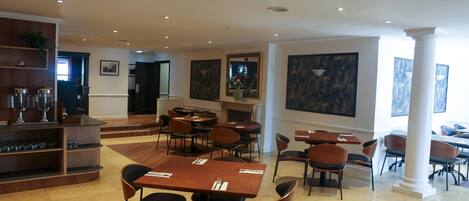 A spacious dining area with multiple tables and chairs, a coffee station, and artwork on the walls.