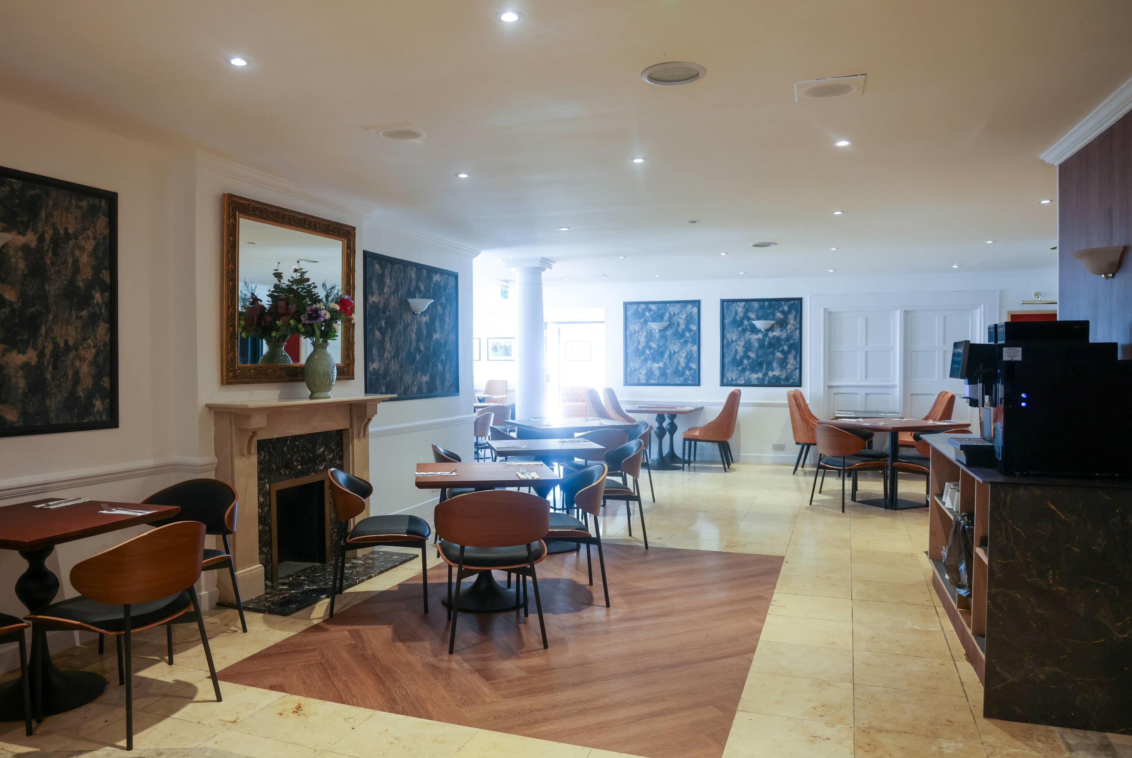 Un comedor de hotel con varias mesas y sillas, una chimenea y obras de arte en las paredes.