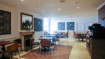 Un comedor de hotel con varias mesas y sillas, una chimenea y obras de arte en las paredes.