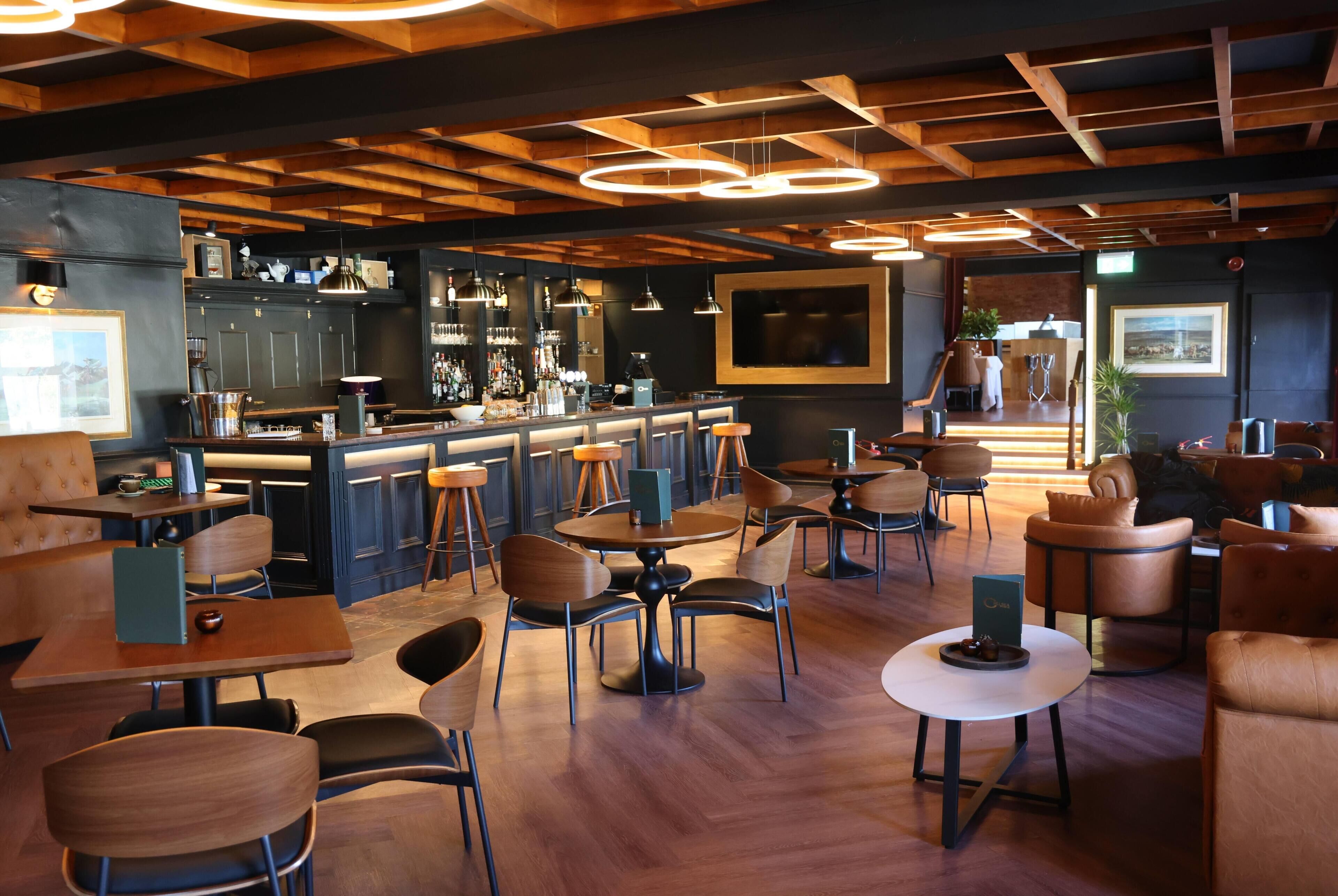 Zona de bar moderna con vigas de madera en el techo, iluminación colgante y una barra con taburetes.