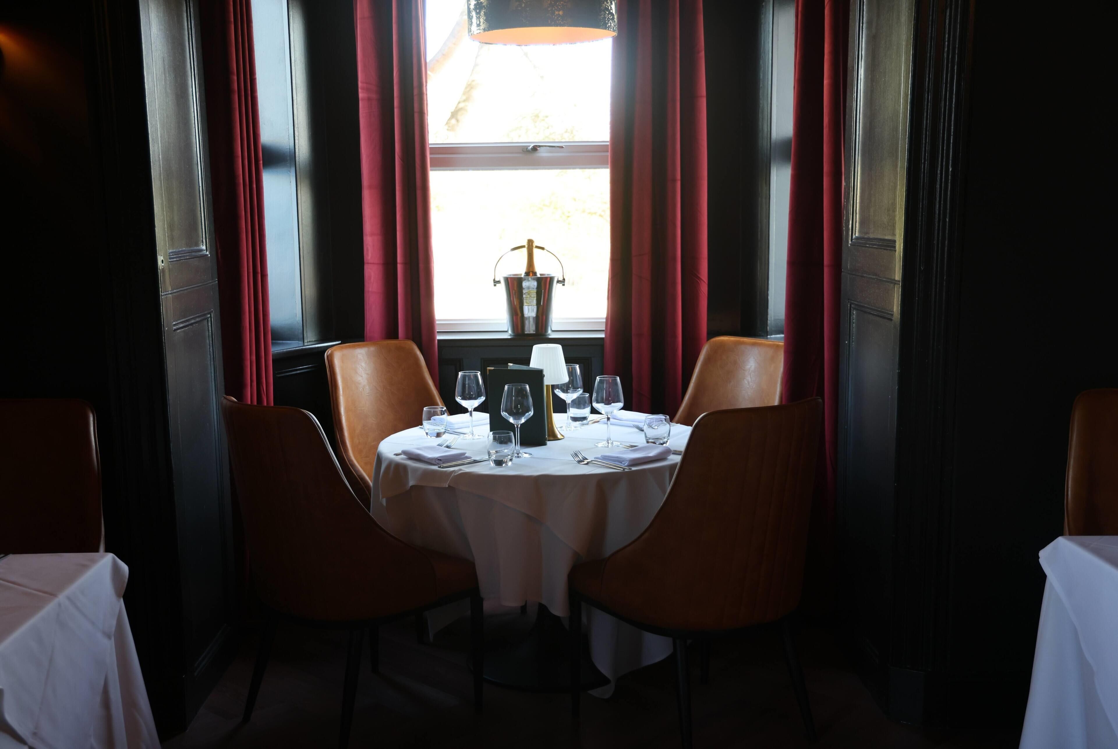 A dining table set for four with a bottle of champagne, glasses, and cutlery.