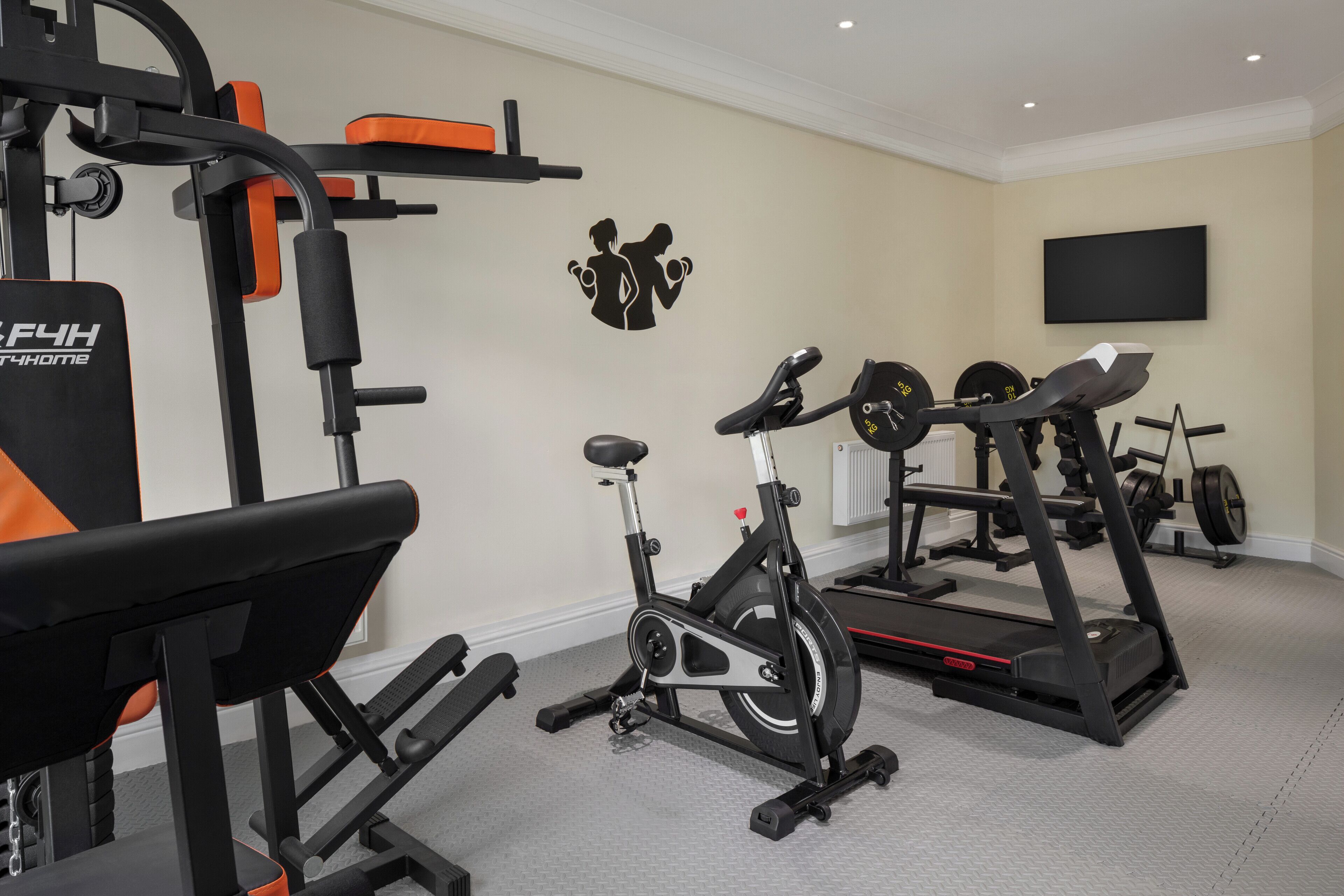 A home gym with exercise equipment including a stationary bike, elliptical, and weight bench.