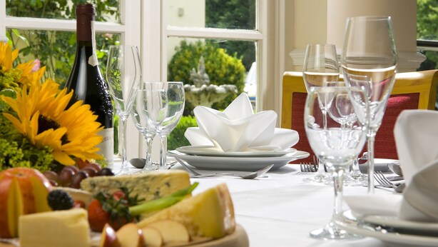 Ein gedeckter Tisch mit Speisen, darunter Wein, Gläser, Teller sowie Käse und Obst.