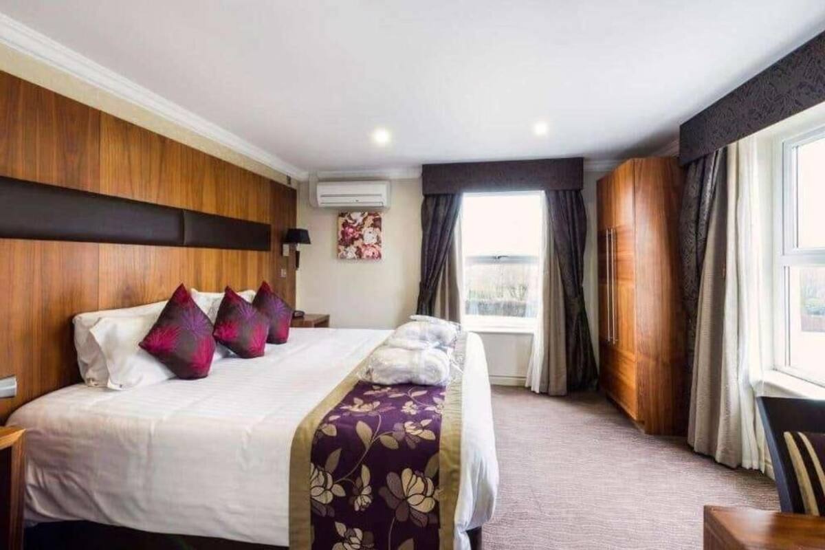 A hotel room with a large bed, a wooden headboard, a window with curtains, and a view of the city.