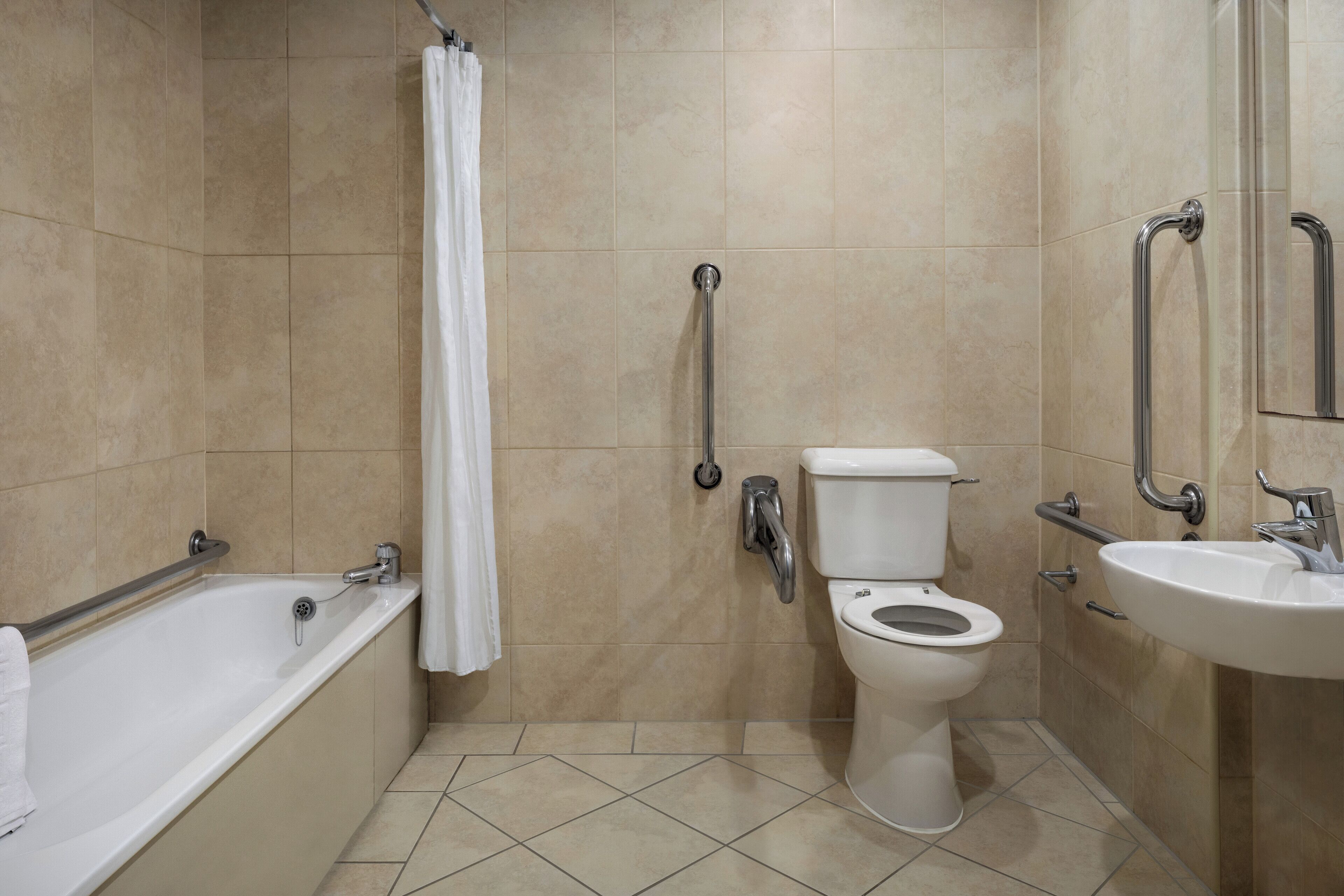 A bathroom with a bathtub, toilet, and sink, equipped with grab bars and a shower curtain.
