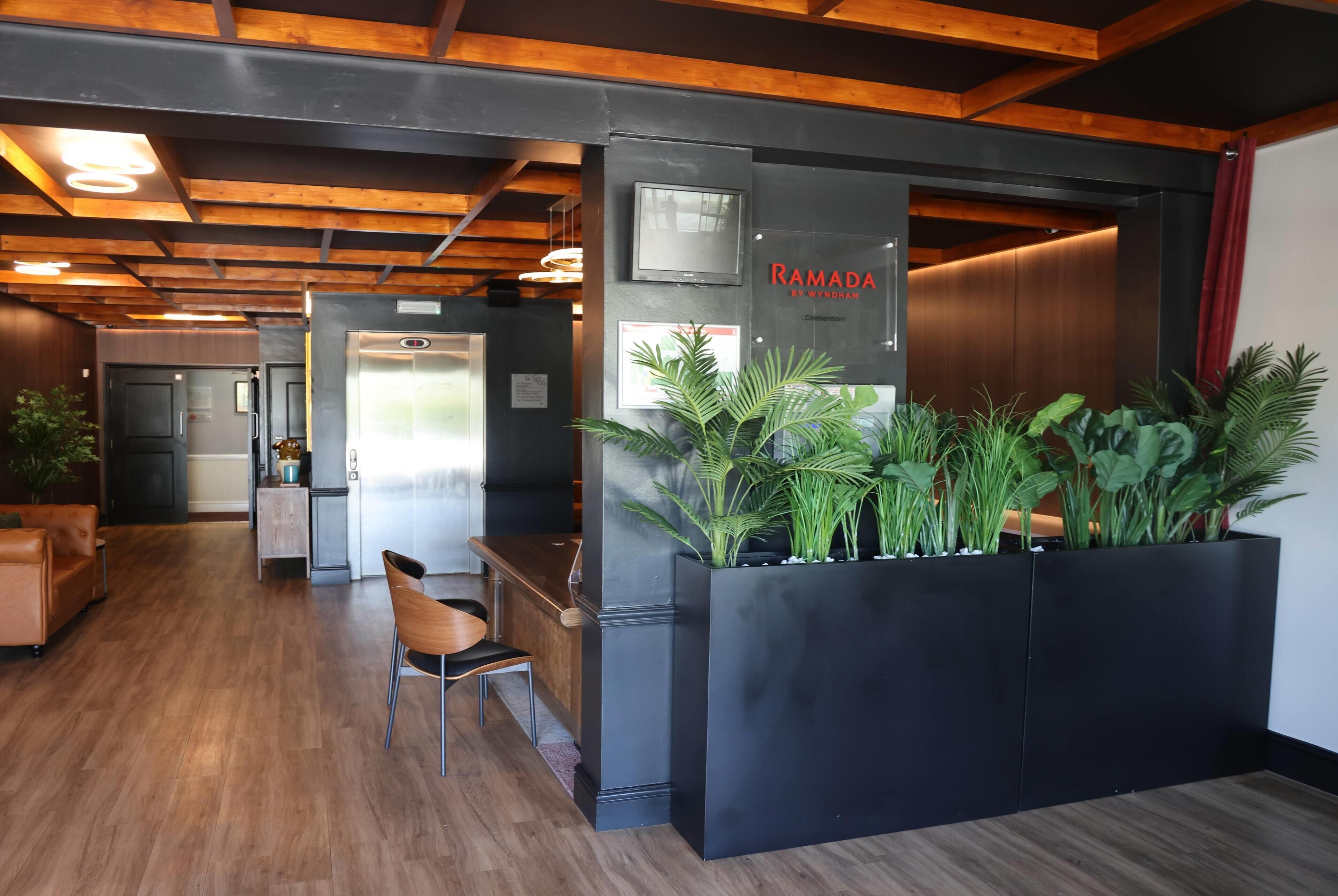 A reception area with a modern design, featuring a black reception desk, a seating area with a chair, and a large planter with green plants.