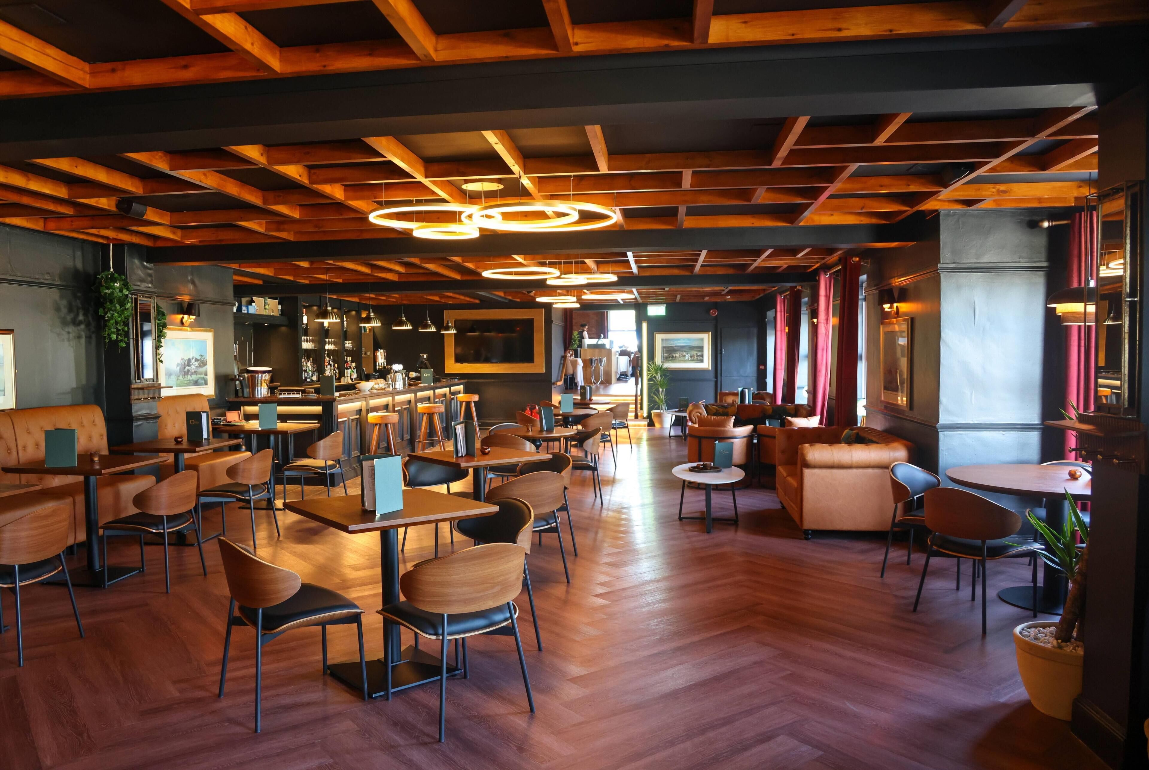A spacious restaurant with wooden flooring, multiple seating areas including tables and booths, and a bar area with a counter.