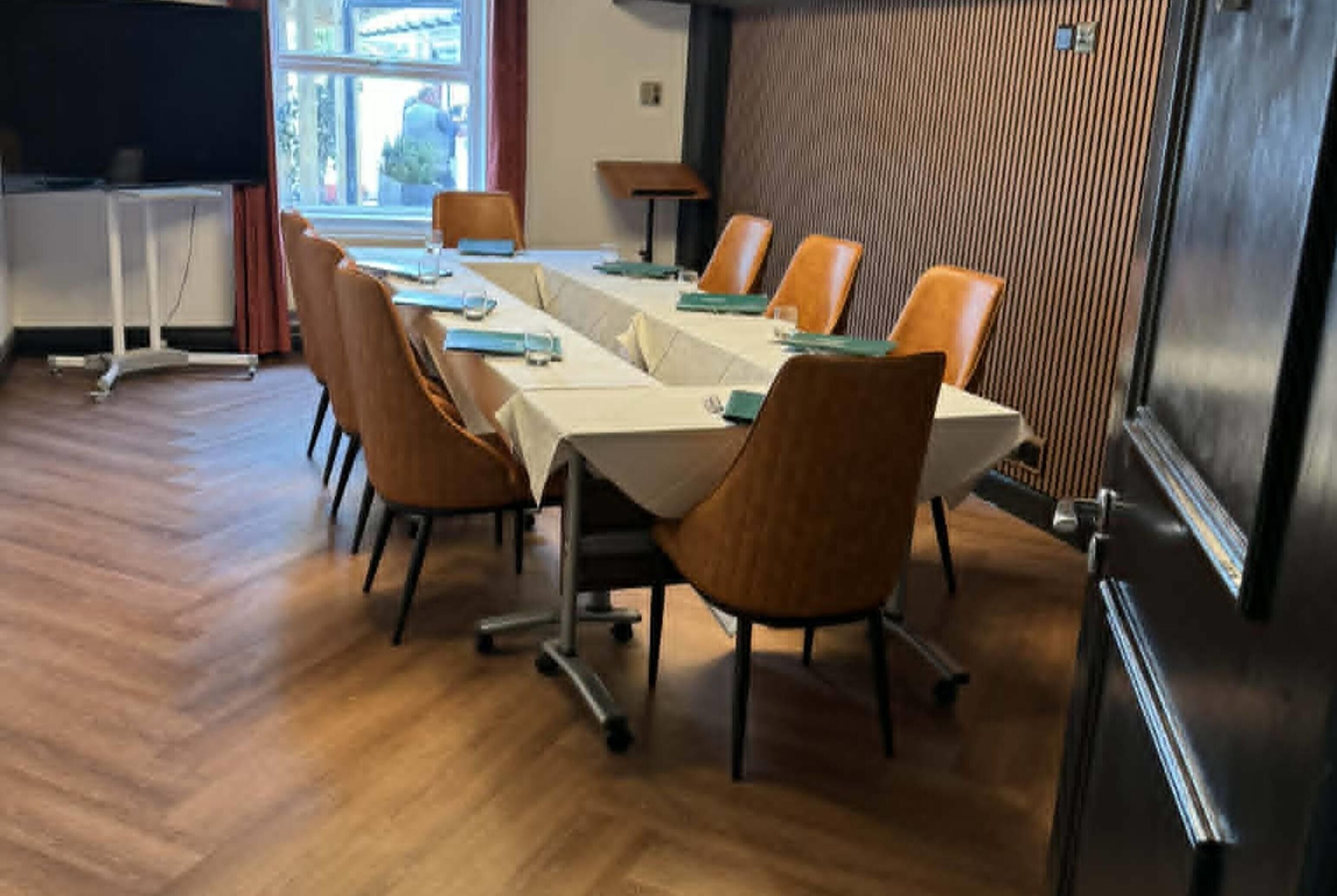 A conference room with a long table, chairs, and a projector screen.