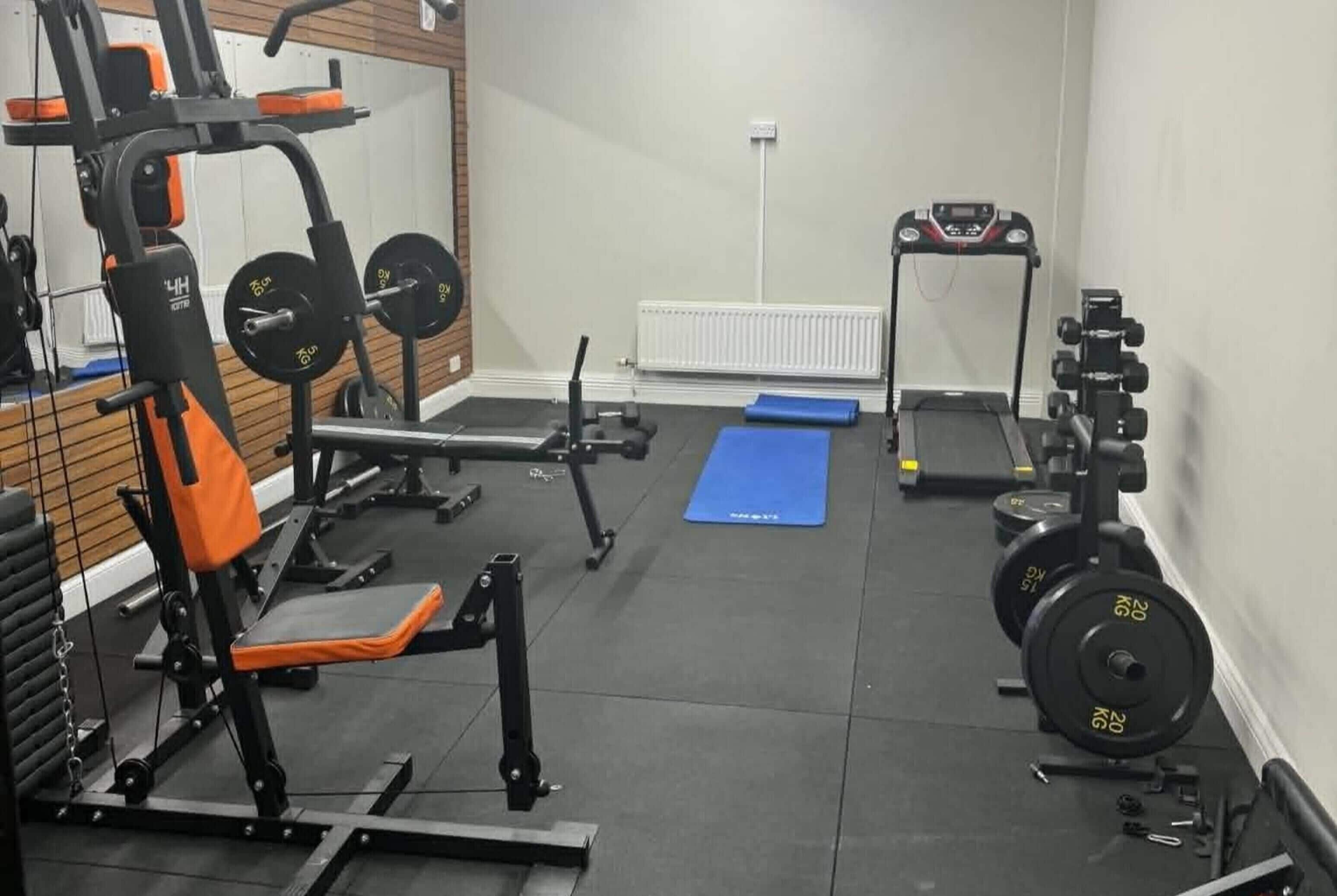 A gym with weightlifting equipment, a treadmill, and a blue mat.