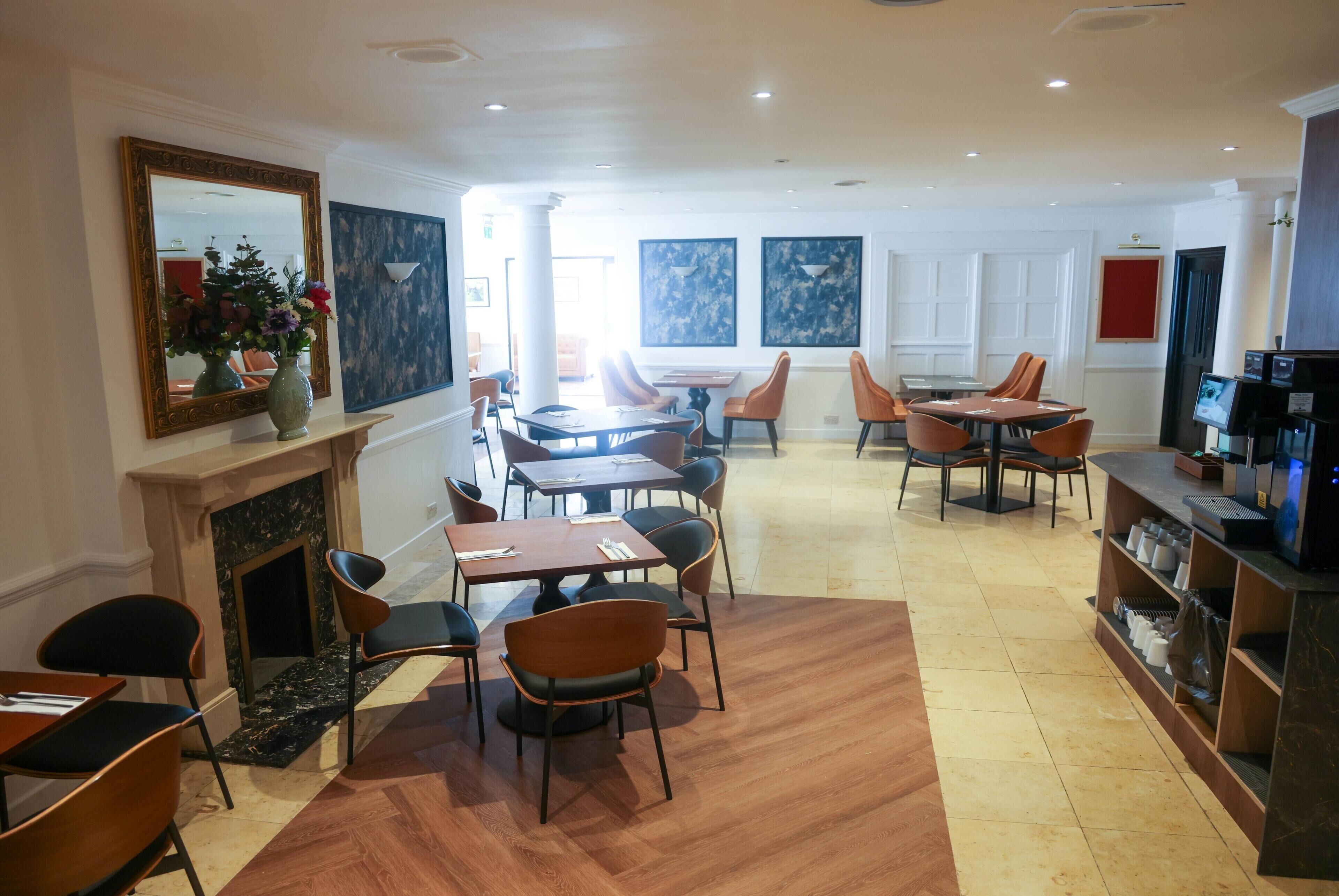A hotel dining area with tables and chairs, a fireplace, and artwork on the walls.