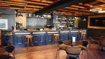 Zona de bar con vigas de madera, taburetes y una barra con diferentes botellas y vasos.