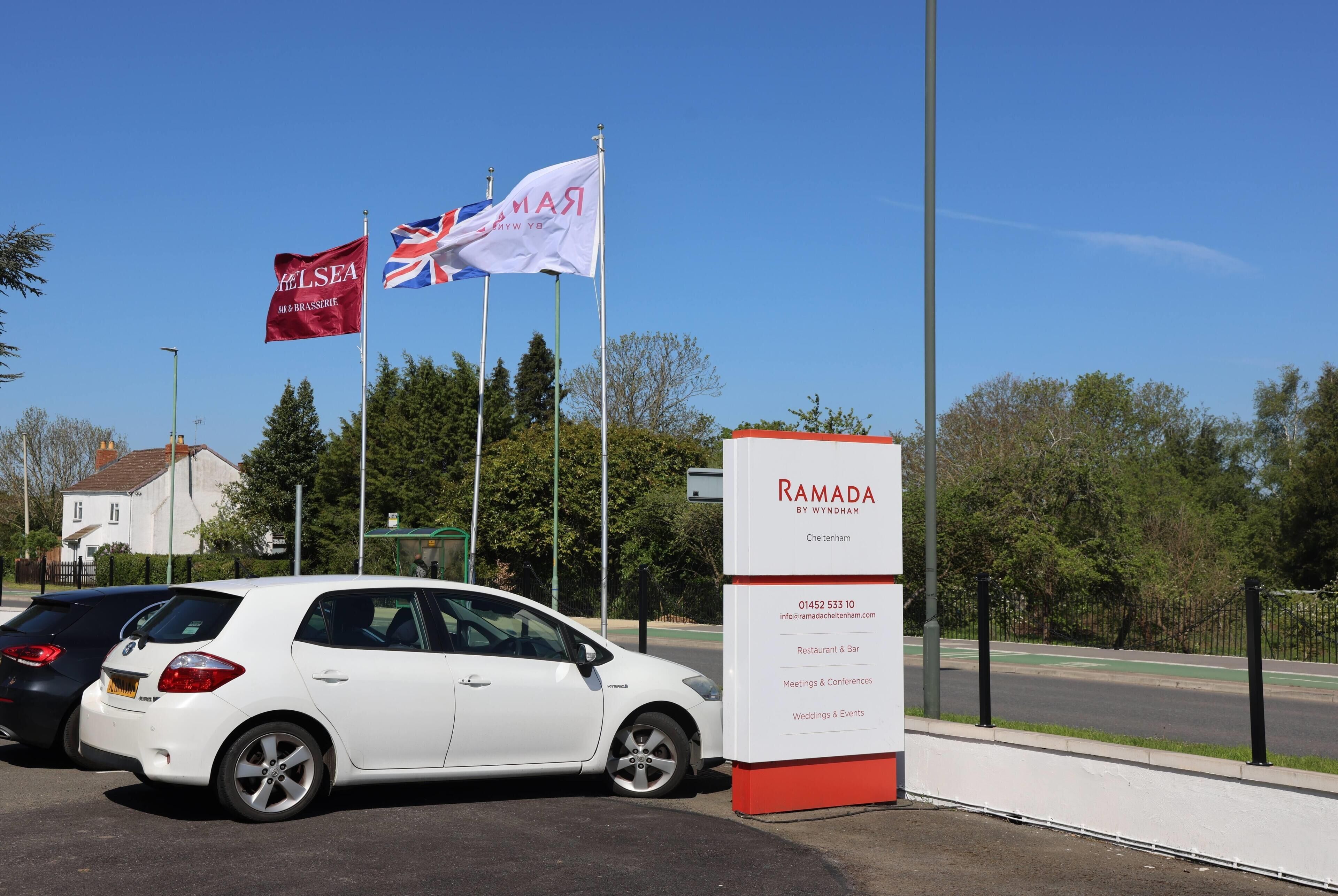 A white car parked in front of a building with a signboard advertising Ramada by Wyndham.