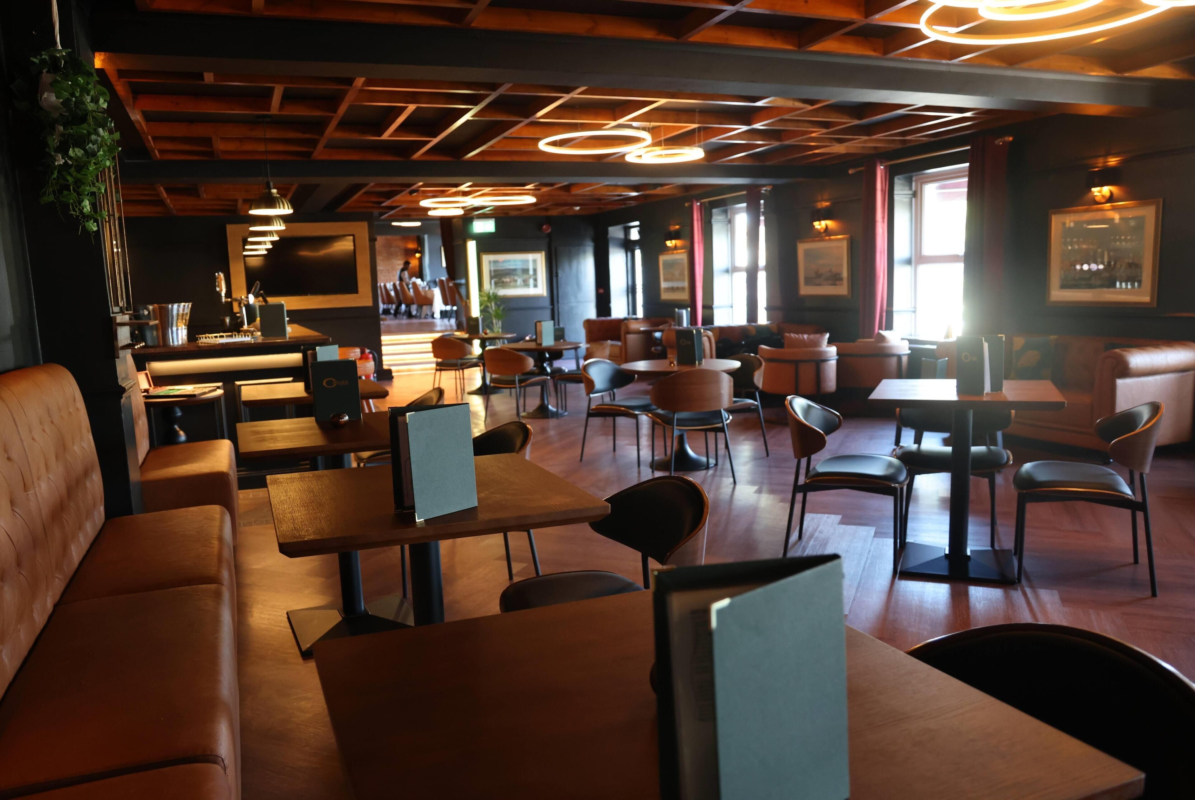Interior de restaurante con mesas y sillas de madera, una zona de bar y obras de arte enmarcadas en las paredes.