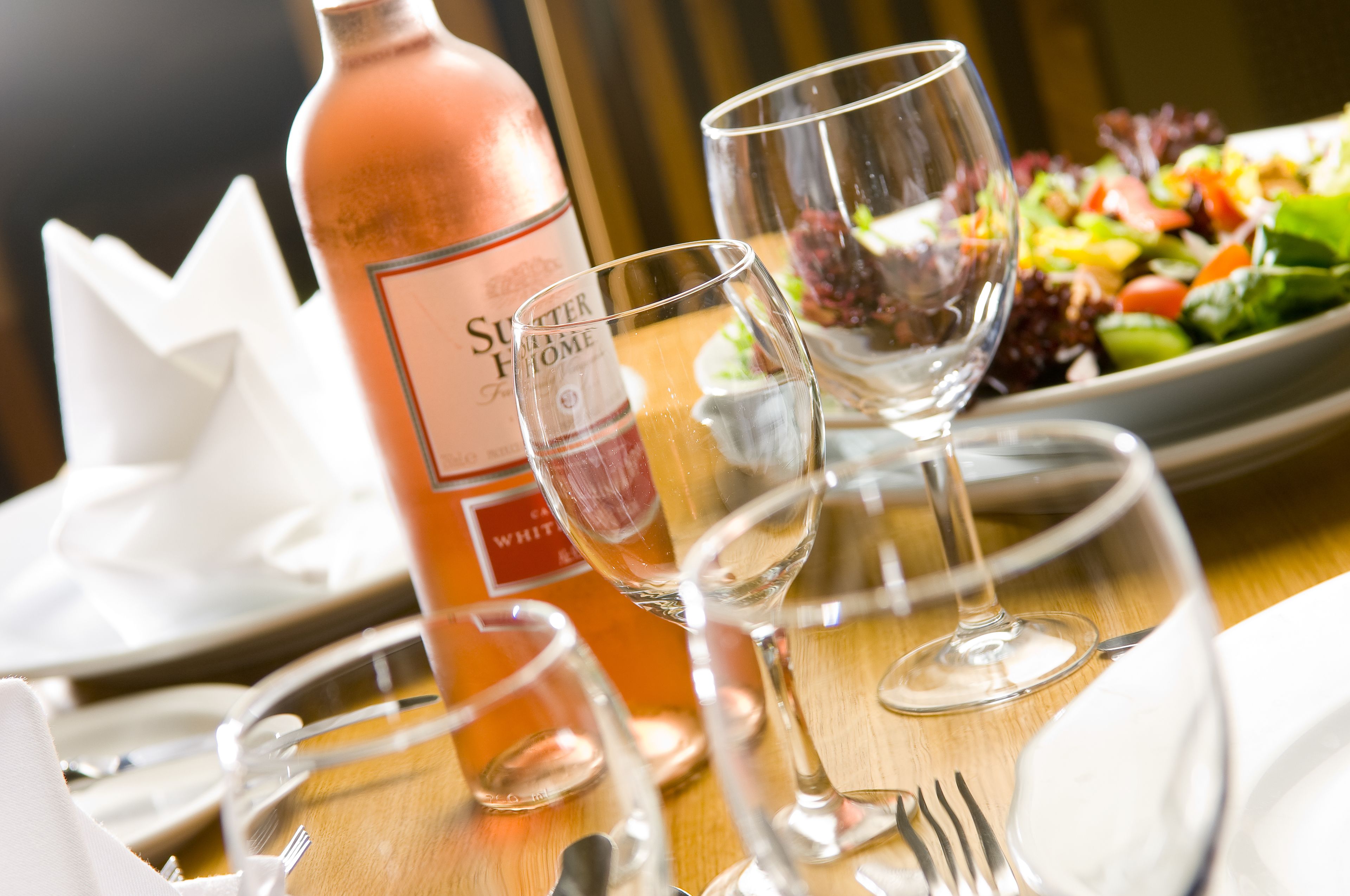 Una mesa dispuesta con una botella de vino blanco, dos copas de vino, una ensalada y cubiertos.