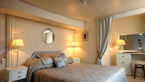 A bedroom with a bed, two bedside tables, a dresser, a mirror, and a window with curtains. - The Gaskell Arms Hotel (Much Wenlock)