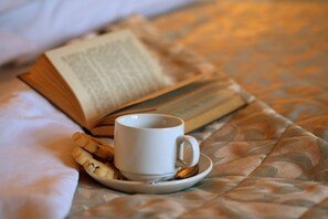 A bed with a blanket, a cup of coffee, a book, and a plate with a pastry. - The Gaskell Arms Hotel (Much Wenlock)