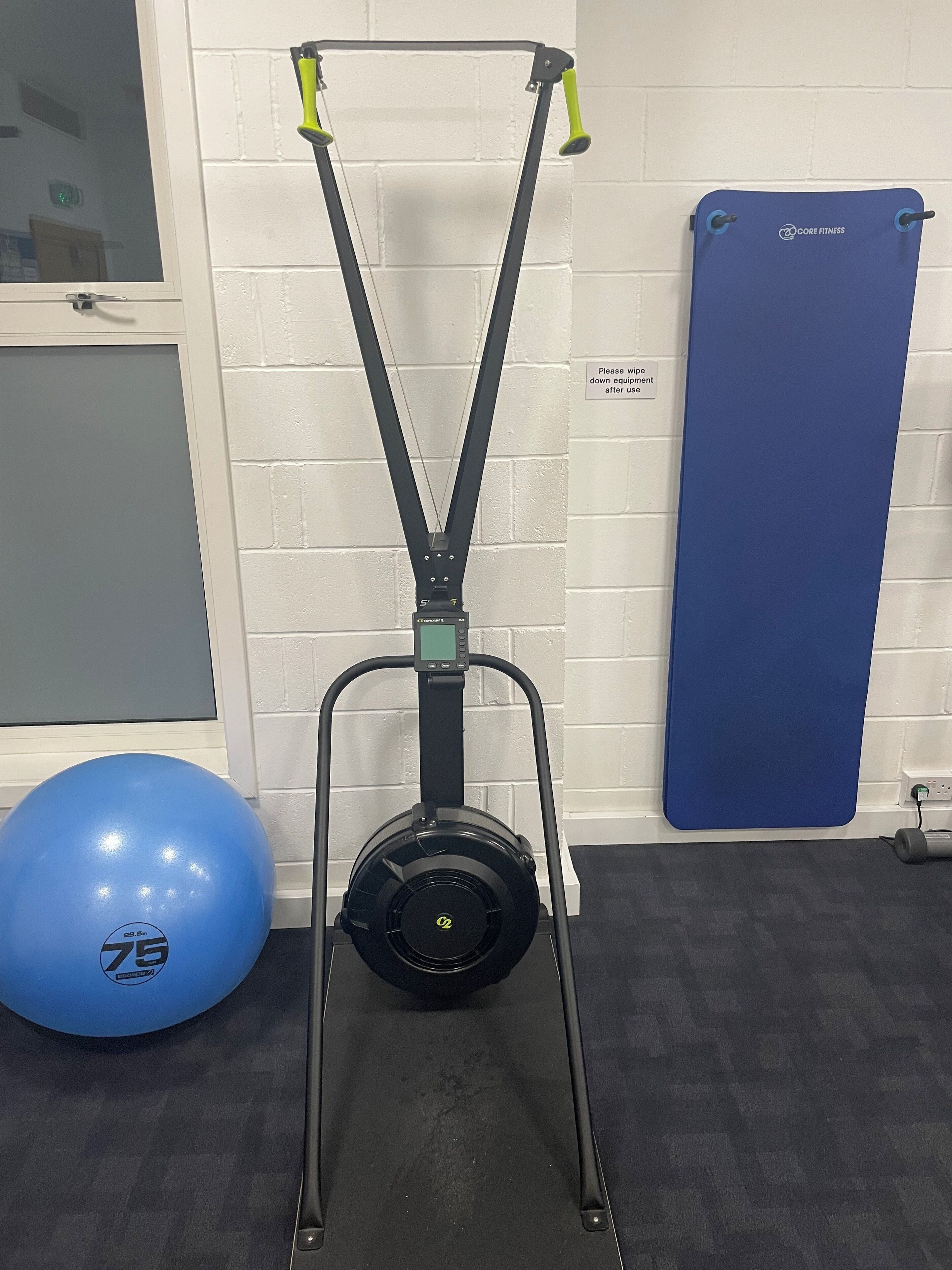 A stationary bike with a digital display, a blue exercise ball, and a blue mat against a white brick wall.