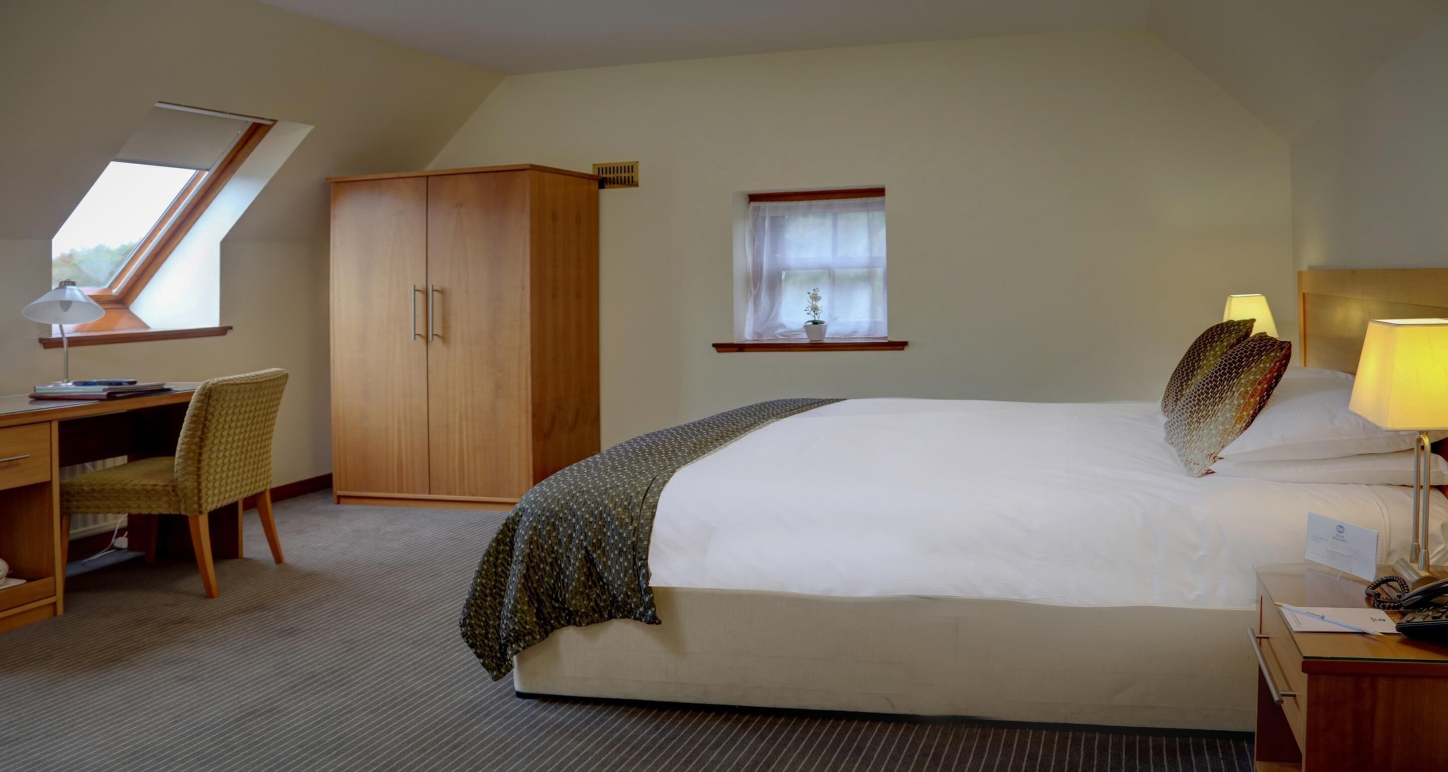 Ein Hotelzimmer mit Bett, Schreibtisch, Stuhl, Kleiderschrank und einem Fenster mit Aussicht.