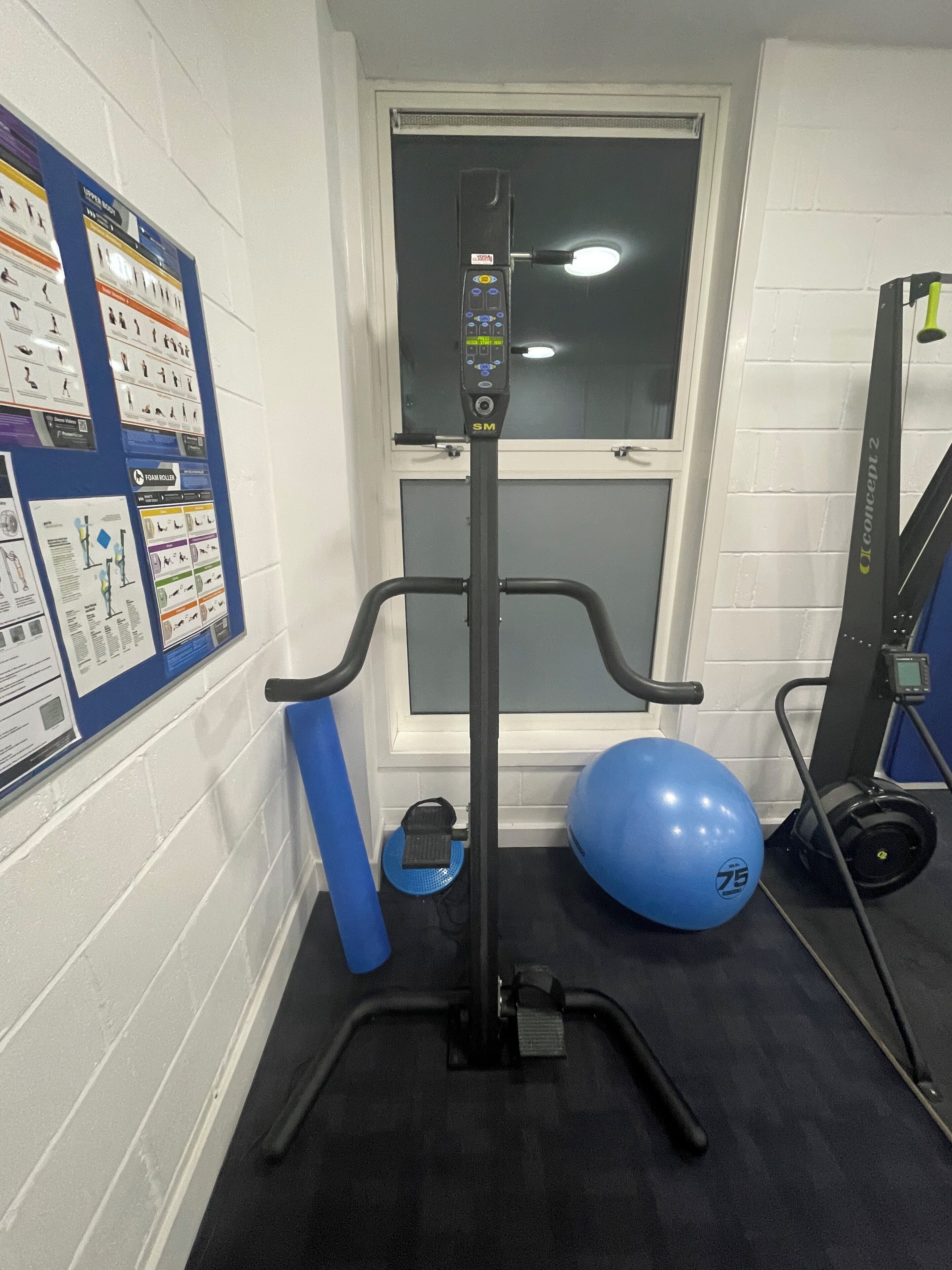 A gym with a stationary bike, a blue exercise ball, and a wall-mounted information board.