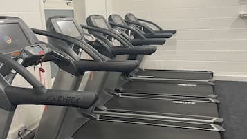 A row of Cybex treadmills in a gym with white brick walls and a window.