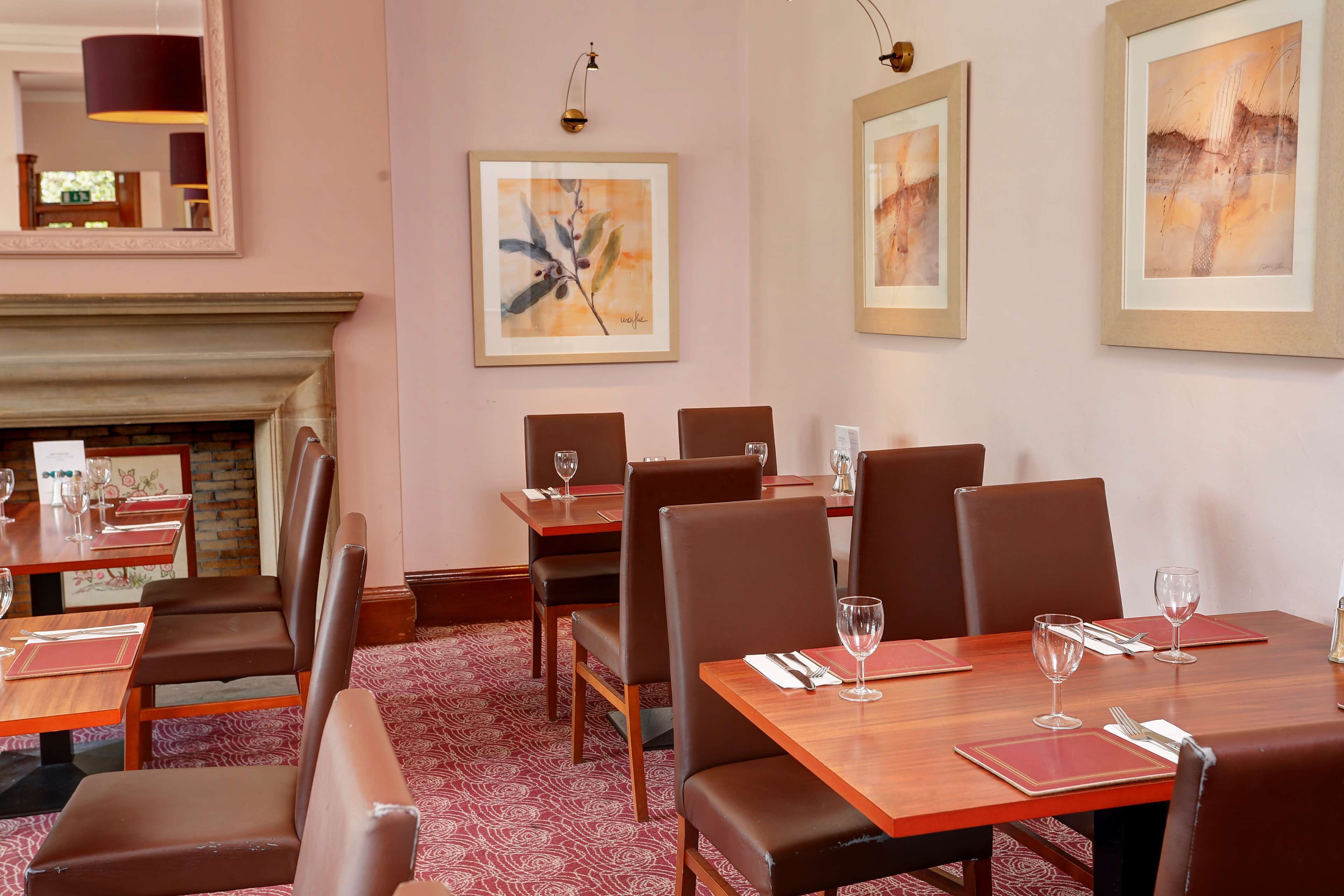 A dining area with wooden tables and brown leather chairs, framed artwork on the walls, and a fireplace.