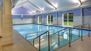 An indoor swimming pool with clear blue water, surrounded by tiled walls and a glass barrier. - Best Western Balgeddie House Hotel (Glenrothes)