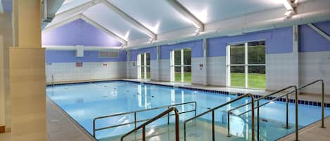 An indoor swimming pool with clear blue water, surrounded by tiled walls and a glass barrier.