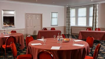 A conference room with round tables, red chairs, and a large window with curtains.