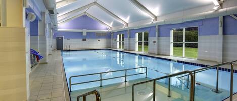 A large indoor swimming pool with clear blue water, surrounded by walls with a blue and white color scheme, and a covered roof structure.