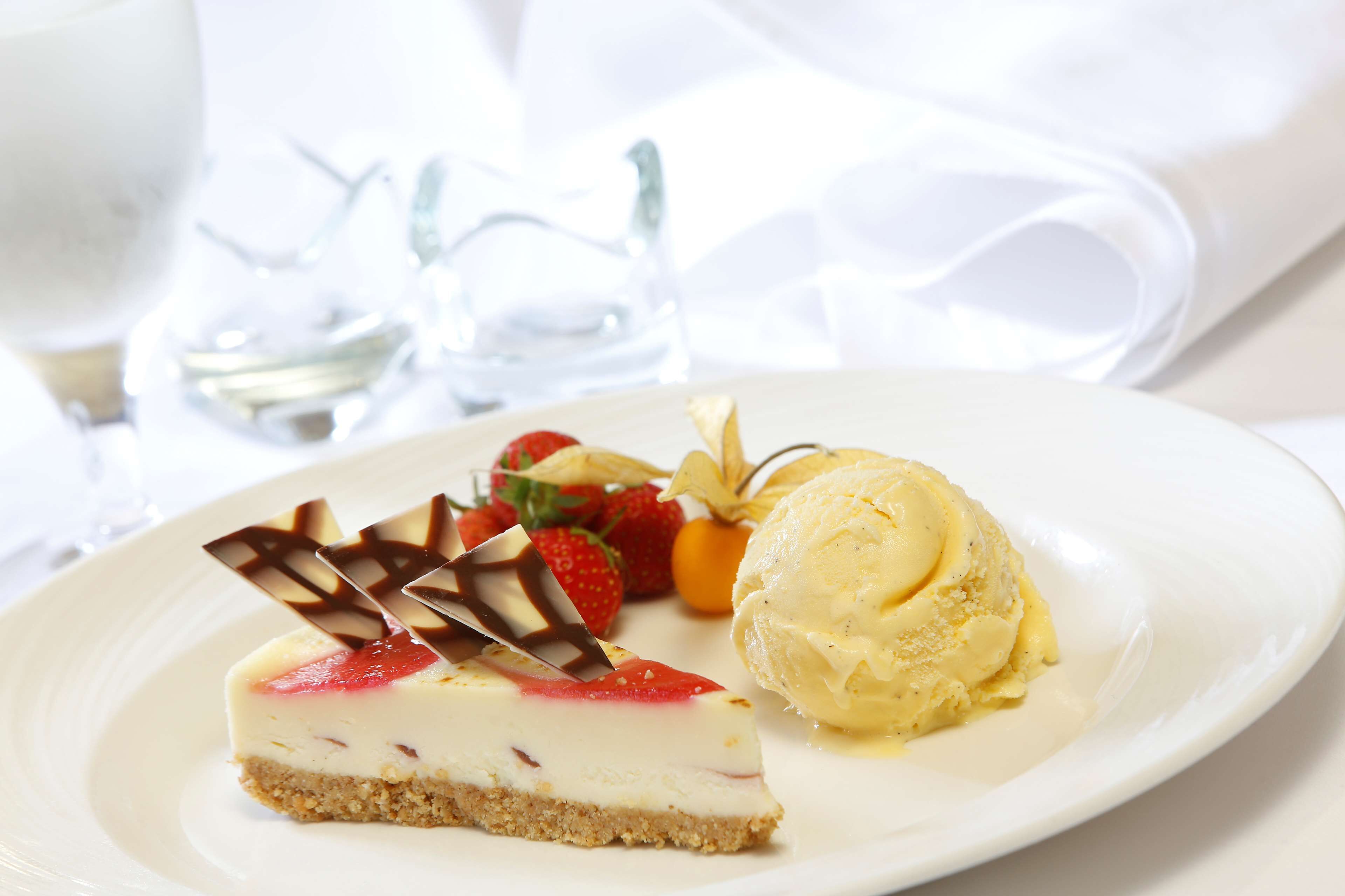 A slice of cheesecake with strawberries and chocolate on a plate, accompanied by a scoop of vanilla ice cream.