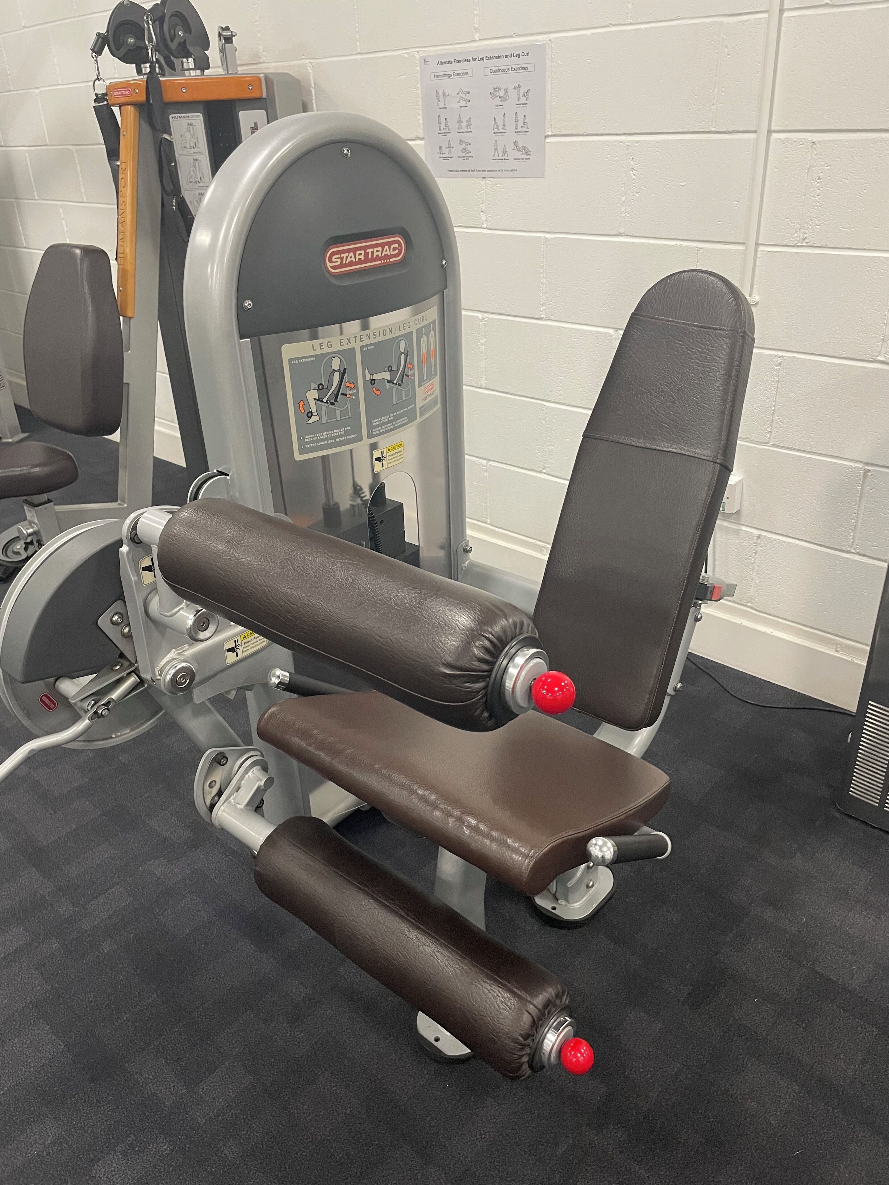 Máquina de extensión y flexión de piernas con banco, una torre de pesas y una máquina de poleas en un gimnasio.