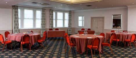 A conference room with multiple tables and chairs, large windows with curtains, and a patterned carpet.