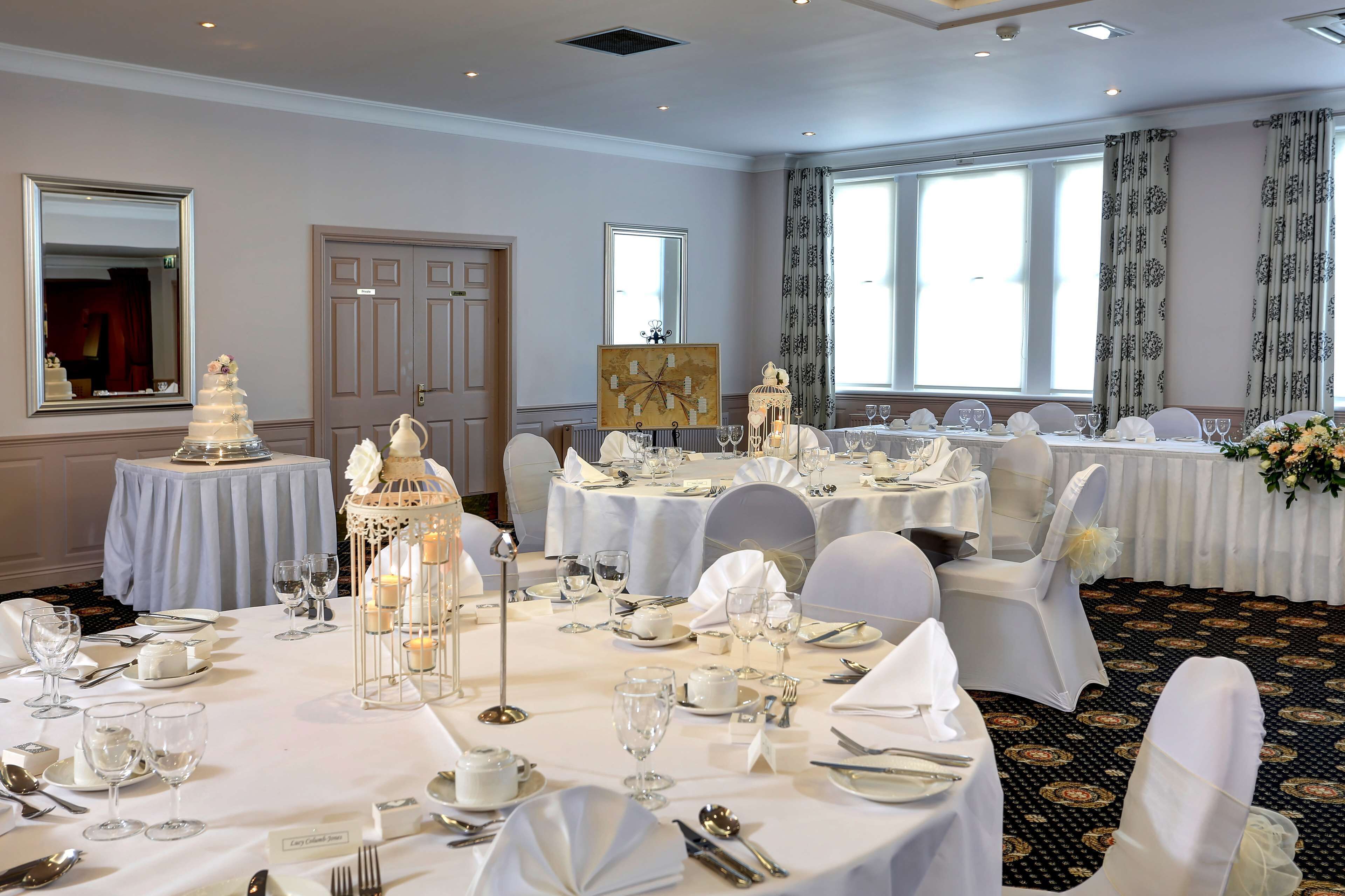 A banquet hall with round tables set for a formal event, featuring white tablecloths, glassware, and floral centerpieces.